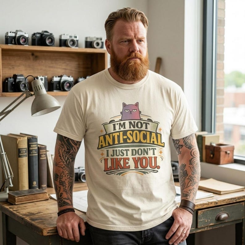 Bearded man in a cozy study wearing the "I'm Not Anti-Social, I Just Don't Like You" sarcastic introvert T-shirt by SarcasmArt in Ivory.