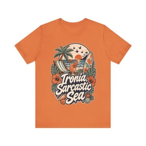 "Ironia, Sarcastic Sea" retro beach T-shirt by SarcasmArt in burnt orange on a plain background, showing a vintage tropical beach scene with palm tree, deck chair, cocktail, surfboard, sunset, hibiscus flowers and shells around the script Ironia, Sarcastic Sea.