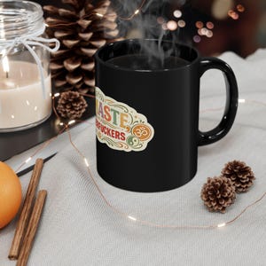 The "Namaste Motherfuckers" funny yoga coffee mug by SarcasmArt steaming with hot coffee in a cozy winter setting with pine cones and cinnamon sticks.