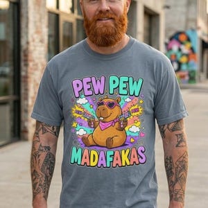Bearded man on a city street wearing the "Pew Pew Madafakas" capybara meme T-shirt by SarcasmArt in Blue Jean.