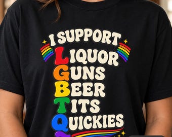 May include: A black t-shirt featuring the text I SUPPORT LIQUOR GUNS BEER TITS QUICKIES in a stacked, colourful design. The letters L, G, B, T, and Q are highlighted in red, orange, yellow, green, and blue, with rainbow accents and stars.