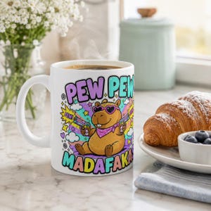The "Pew Pew Madafakas" capybara coffee mug by SarcasmArt on a breakfast table with a croissant and berries – a meme mug for capybara lovers.