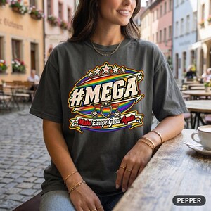 Woman with a coffee at a street café wearing the "#MEGA Make Europe Great Again" Rainbow Pride T-shirt by SarcasmArt in Pepper.