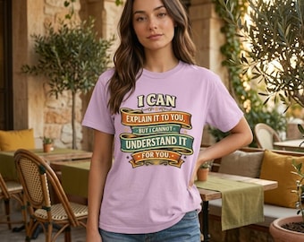 May include: A light purple short-sleeve t-shirt featuring a graphic with the text I CAN EXPLAIN IT TO YOU, BUT I CANNOT UNDERSTAND IT FOR YOU. The design includes layered orange, teal, and yellow banners with decorative flourishes.