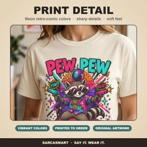 Print detail of the "Pew Pew Madafakas" raccoon meme T-shirt by SarcasmArt: bold retro neon colors, sharp details and a soft feel on garment-dyed cotton.