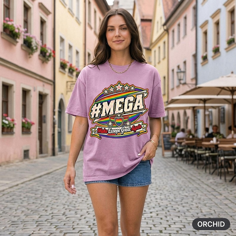 Woman on a sunny European old-town street wearing the "#MEGA Make Europe Great Again" Rainbow Pride T-shirt by SarcasmArt in Orchid – a satirical #MEGA collection shirt with a retro #MEGA sports badge with rainbow pride stripes, a rainbow heart shield, stars and a Make Europe Great Again script banner.