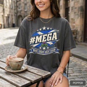 Woman with a coffee at an outdoor café table wearing the "#MEGA Make Europe Great Again" Scotland T-shirt by SarcasmArt in Pepper.