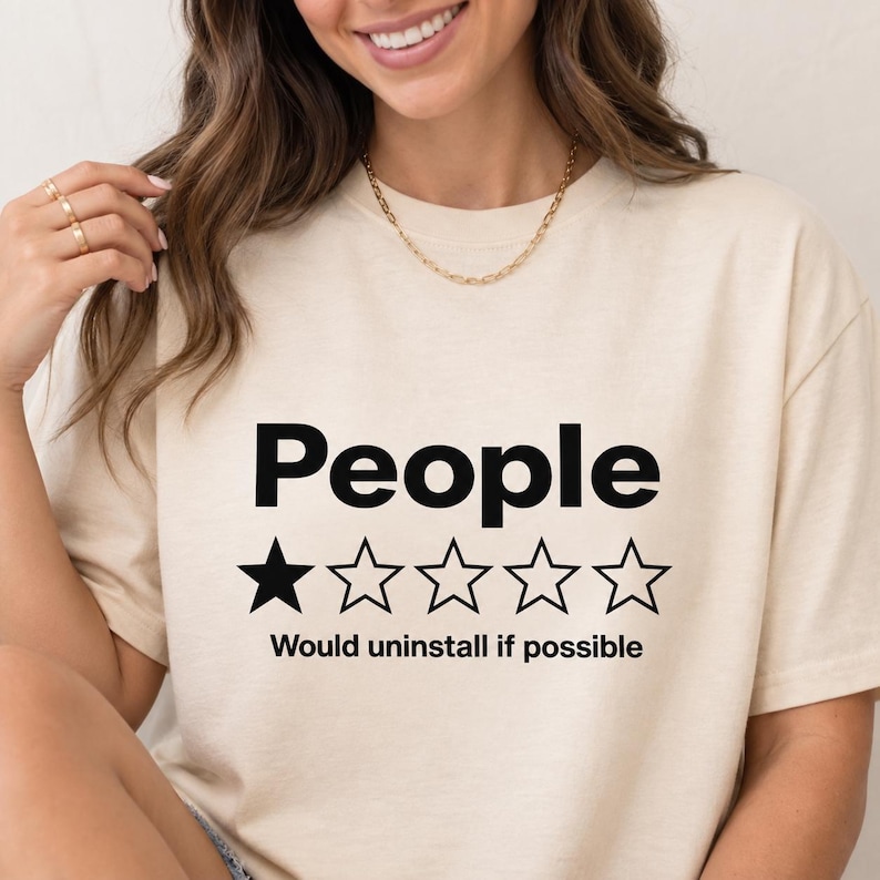 Close-up of the "People – 1 Star, Would Uninstall If Possible" funny review T-shirt by SarcasmArt in Natural worn by a woman – a Bella+Canvas 3001 unisex tee with the word People with a one-out-of-five-star rating and the review Would uninstall if possible in black.