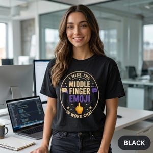 Smiling woman at her workstation wearing the "I Miss the Middle Finger Emoji in Work Chat" sarcastic office T-shirt by SarcasmArt in Black.