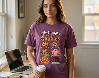 May include: A purple t-shirt featuring the text "Yes I accept all Cookies" above six illustrated cookie varieties, including chocolate chip, blueberry, oatmeal raisin, sugar, peanut butter, and double chocolate, each with its own label.