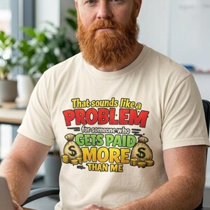 Bearded man at his desk with a laptop and mug wearing the "That Sounds Like a Problem for Someone Who Gets Paid More Than Me" sarcastic coworker T-shirt by SarcasmArt in Ivory.