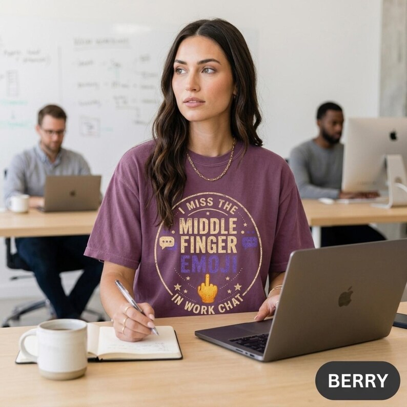 Woman taking notes at an office desk with a laptop, wearing the "I Miss the Middle Finger Emoji in Work Chat" sarcastic office T-shirt by SarcasmArt in Berry.