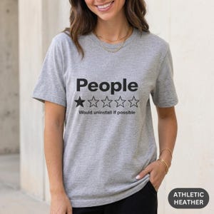 Woman wearing the "People – 1 Star, Would Uninstall If Possible" funny review T-shirt by SarcasmArt in Athletic Heather (grey).