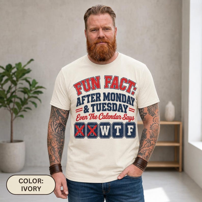 Bearded man wearing the "Fun Fact: After Monday & Tuesday" WTF varsity work T-shirt by SarcasmArt in Ivory, showing the red and navy varsity print.