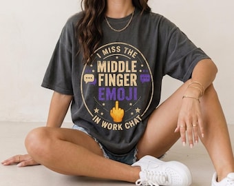 Può includere: Una t-shirt grigio antracite a maniche corte con una grafica circolare recante il testo I MISS THE MIDDLE FINGER EMOJI IN WORK CHAT. Il design include un'emoji gialla del dito medio, fumetti viola e piccole stelle in stile vintage.