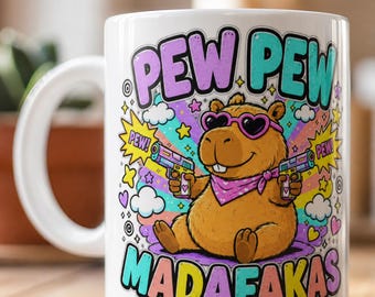 Op de afbeelding: Een witte keramische mok met een cartoon capibara die een hartvormige zonnebril en een roze bandana met stippen draagt. De capibara houdt twee speelgoedpistolen vast. De tekst luidt PEW PEW MADAFAKAS met sterren, wolken en een regenboog.