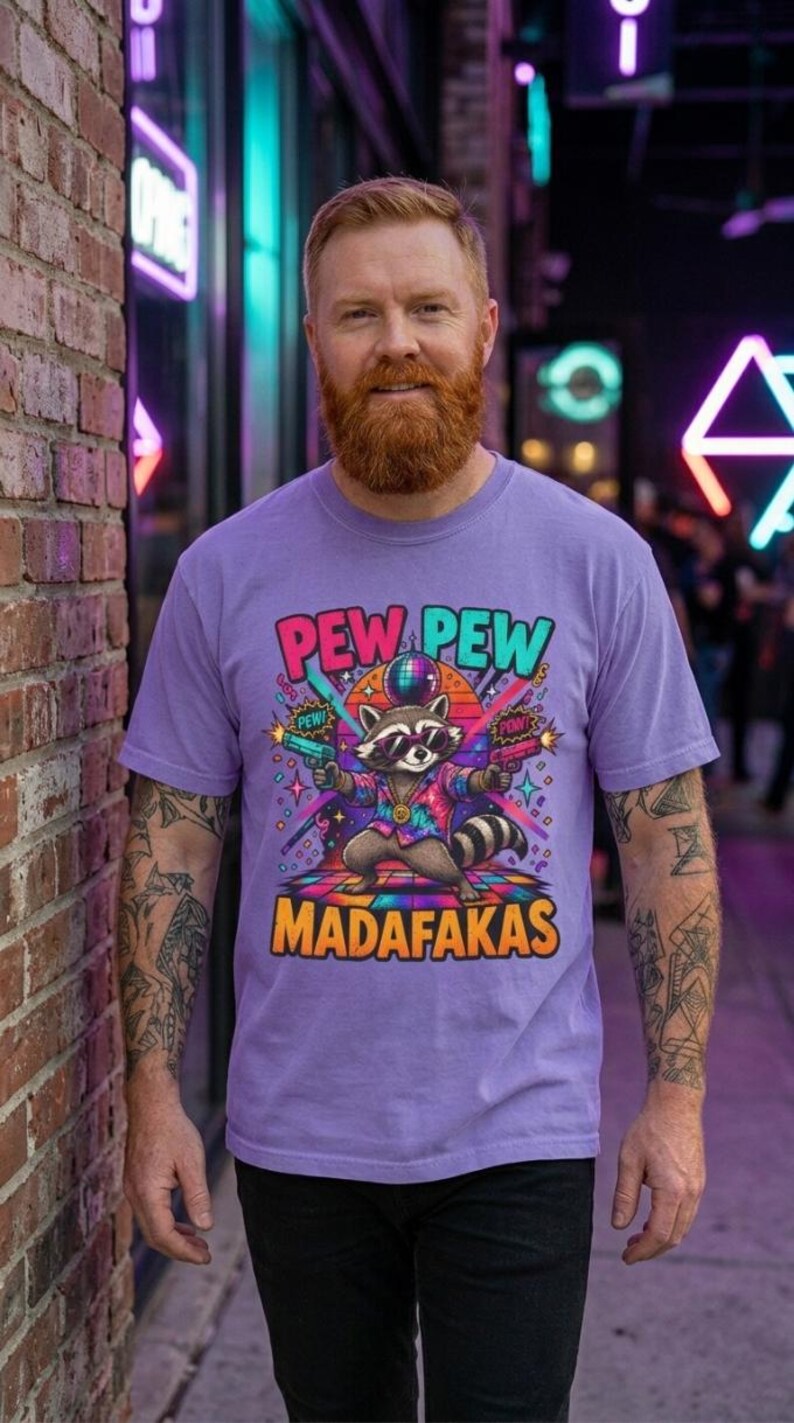 Bearded man in front of a neon-lit brick wall wearing the "Pew Pew Madafakas" raccoon meme T-shirt by SarcasmArt in Violet.