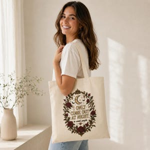 Smiling woman carrying the Natural "I Only Come Out at Night to Avoid People" gothic canvas tote bag by SarcasmArt over her shoulder – a gothic introvert gift.