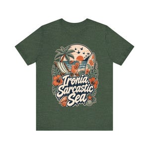 "Ironia, Sarcastic Sea" retro beach T-shirt by SarcasmArt in olive green on a plain background, showing a vintage tropical beach scene with palm tree, deck chair, cocktail, surfboard, sunset, hibiscus flowers and shells around the script Ironia, Sarcastic Sea.