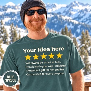 Bearded man in a beanie and sunglasses in front of snowy mountains wearing the personalized golden 5-star review T-shirt by SarcasmArt in Blue Spruce, with your custom title, five golden stars and four lines of your own review text in white.