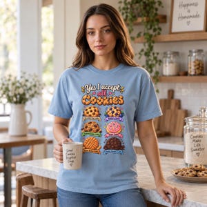 Woman holding a mug in a bright kitchen wearing the "Yes, I Accept All Cookies" funny programmer T-shirt by SarcasmArt in Chambray (light blue).