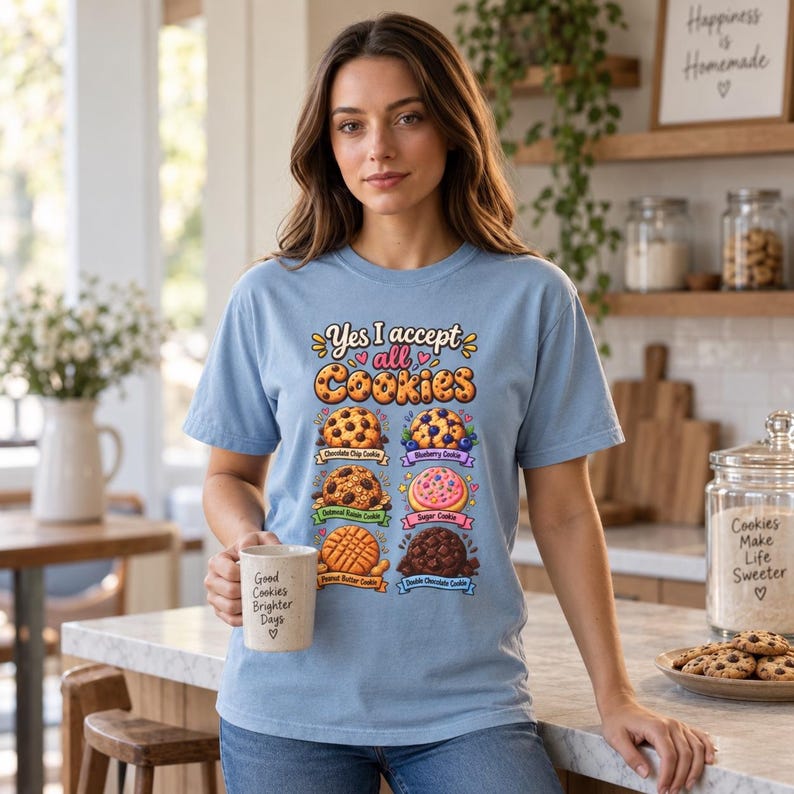 Woman holding a mug in a bright kitchen wearing the "Yes, I Accept All Cookies" funny programmer T-shirt by SarcasmArt in Chambray (light blue).