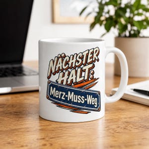 May include: A white ceramic mug featuring a graphic design with the text NÄCHSTER HALT: Merz-Muss-Weg. The design includes orange brush strokes and a blue rectangular sign with white lettering, mimicking a public transit stop sign.