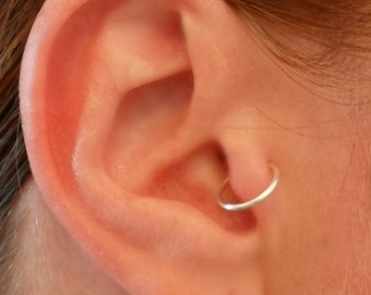 May include: A close-up of a person's ear with a small silver hoop earring in the helix piercing.