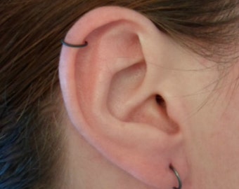 Puede incluir: Una oreja con dos pequeños aros negros. Los aros están en el lóbulo superior de la oreja y el hélix.