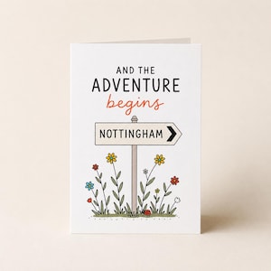 Peut inclure: Une carte de vœux blanche avec le texte noir AND THE et le texte orange begins, avec le mot ADVENTURE en noir. En dessous se trouve un panneau de signalisation pointant vers la droite avec l'inscription NOTTINGHAM, entouré de fleurs colorées.