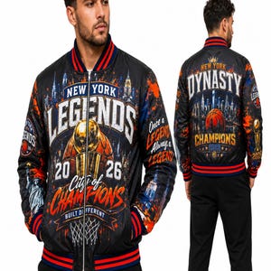 Puede incluir: Una chaqueta bomber negra con un gráfico del horizonte de Nueva York, un trofeo de baloncesto y el texto "New York Legends City of Champions 2026" en el frente, con "Dynasty Champions 2026" y un gráfico de baloncesto en la espalda.