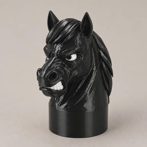 May include: A glossy black horse head figurine with a cylindrical base. The horse has a sculpted mane, pointed ears, and a fierce expression with bared white teeth and visible white eyes. The surface is smooth and reflective, showing detailed features.
