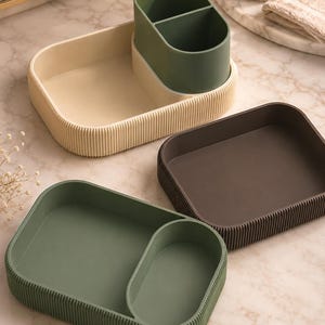 May include: Three rectangular storage organisers with rounded corners and vertical ribbed exterior walls. One organiser is cream with a dark green divided insert, one is dark brown, and one is sage green with a matching divided section.