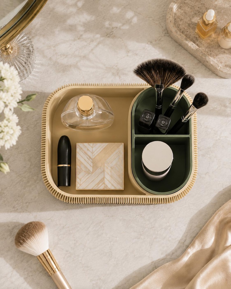 May include: A beige rectangular vanity organiser tray with a ribbed outer edge, featuring a separate dark green compartment for brushes and small items. The tray holds a clear perfume bottle, a black lipstick, a square compact, and brushes.