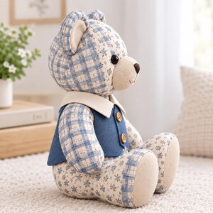 K&ouml;nnte beinhalten: Ein Stoffteddyb&auml;r aus blau-wei&szlig; kariertem Stoff und einem Blumenmuster. Der B&auml;r tr&auml;gt eine einfarbige blaue Weste mit zwei braunen Kn&ouml;pfen und einem cremefarbenen Kragen. Er hat schwarze Knopfaugen und eine hellbeige Schnauze.