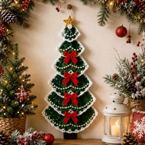 May include: A wall-hanging crochet Christmas tree decoration in dark green with white scalloped edges. The tree features five tiers, each adorned with a small red fabric bow and a string of white faux pearls. A gold crocheted star sits at the top.