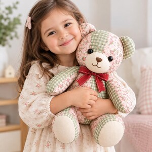 May include: A plush teddy bear featuring a patchwork design of light green gingham fabric and a pink floral print fabric. The bear has black button eyes, a stitched nose and mouth, and a dark red ribbon tied in a bow around its neck.