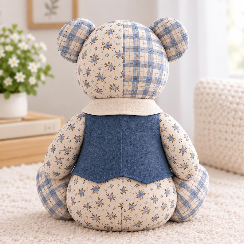 K&ouml;nnte beinhalten: Ein Stoffb&auml;r im Patchwork-Design aus cremefarbenem Stoff mit kleinen blauen Blumen und einem blau-wei&szlig;en Karomuster. Der B&auml;r tr&auml;gt eine einfarbige dunkelblaue Weste &uuml;ber einem cremefarbenen Kragen, von hinten betrachtet.