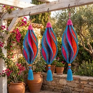 May include: Three hanging spiral ornaments featuring a vibrant crochet design in shades of hot pink, orange, and bright blue. Each piece is topped with a matching crochet loop and finished at the bottom with a decorative bead and a long tassel.