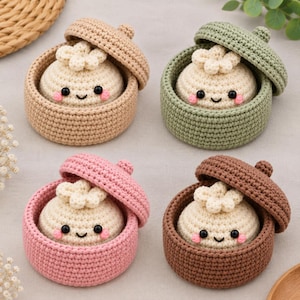 May include: Four crocheted dumpling toys, each nestled in a matching lidded container. The dumplings are cream-colored with black bead eyes and pink cheeks. The containers come in beige, sage green, soft pink, and brown, all featuring a textured stitch.