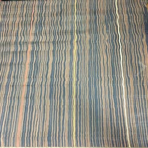 May include: A rectangular textile with a striped pattern. The stripes are vertical and wavy, in shades of blue, tan, and peach, with a few yellow and white stripes. The fabric appears to be folded or slightly wrinkled.