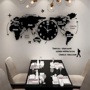Puede incluir: Un reloj de pared negro integrado en un vinilo de pared de mapa mundial con continentes, océanos e iconos de aviones. El texto dice: There is a whole world outside waiting for me I have to take a look. Incluye la silueta de una persona.