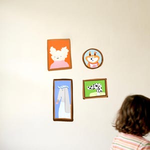 Può includere: Quattro adesivi da parete con personaggi animali illustrati in cornici. Una cornice rettangolare mostra una creatura bianca su sfondo arancione, una circolare una volpe arancione, una alta un coniglio grigio e una quadrata un cane maculato.