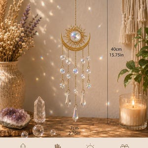 May include: A gold-toned sun and crescent moon suncatcher featuring a central iridescent crystal, hanging chains, and clear crystal prisms. The ornament measures 15.75 inches in height and 2.76 inches in width, suspended by a thin metal chain.