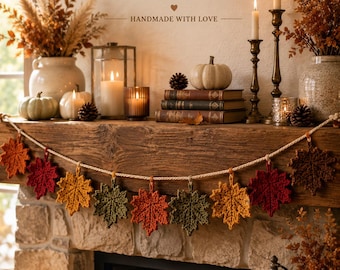 May include: A crochet pattern for a maple leaf garland featuring the text MAPLE LEAF GARLAND Crochet Pattern HANDMADE WITH LOVE. The garland consists of individual crocheted maple leaves in shades of red, orange, yellow, and green, strung together on a light-colored cord.
