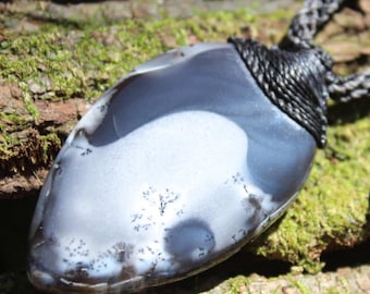 May include: A teardrop-shaped gray and white dendritic agate pendant featuring dark fern-like inclusions. The stone is secured by a black macrame cord with a braided texture and a small metallic bead accent near the adjustable closure.