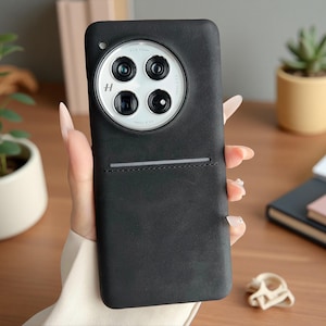 May include: A matte black smartphone case with a smooth texture, featuring a large circular camera module at the top with four lenses and the letter H logo. A horizontal stitched pocket detail is positioned below the camera housing.