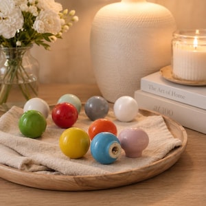 May include: A collection of ten spherical cabinet knobs in various solid colors including white, green, red, light blue, gray, orange, yellow, and pink. Each knob features a smooth, glossy finish and a central metal threaded hole for installation.