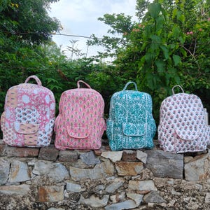 Peut inclure: Quatre sacs à dos matelassés disposés en rangée, chacun présentant un motif floral ou patchwork distinct. Le premier est un modèle patchwork rose et blanc, le deuxième est rose avec de petits motifs floraux, le troisième est bleu sarcelle et le quatrième est blanc.
