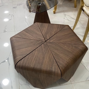 Könnte beinhalten: Ein niedriger, sechseckiger Couchtisch aus dunkelbraunem Holz mit sichtbarer Maserung. Die Tischplatte besteht aus sechs dreieckigen Segmenten, die in einem Mittelpunkt zusammenlaufen und geschwungene Kanten haben, die bis zum Boden reichen.